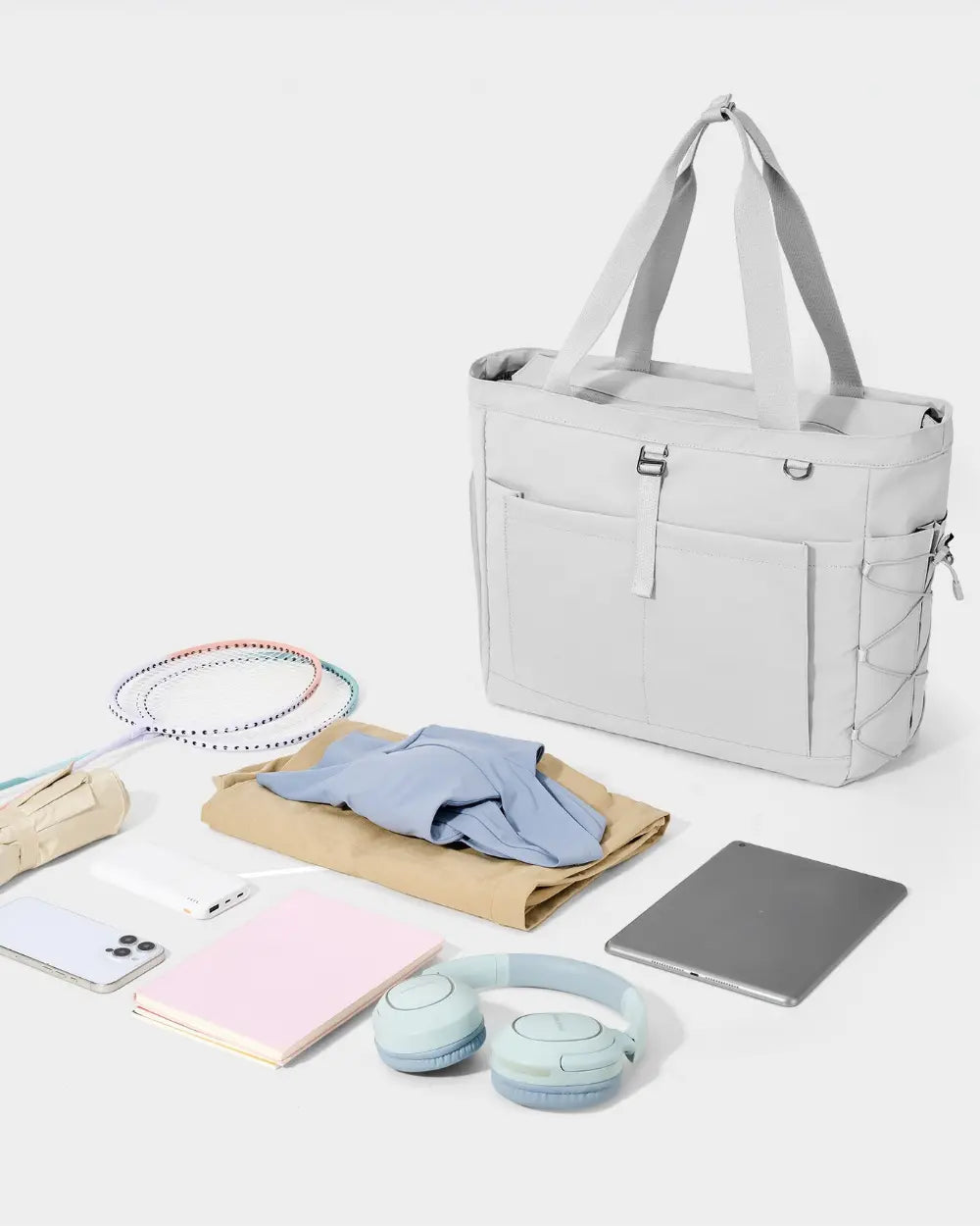 Gray tote bag with various items including a phone, tablet, and headphones on a light background